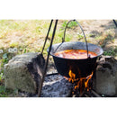 Enameled Dutch oven hanging over campfire cooking stew outdoors with stones supporting the firepit