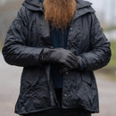 Person wearing black tactical leather gloves and a black jacket outdoors with a blurred background