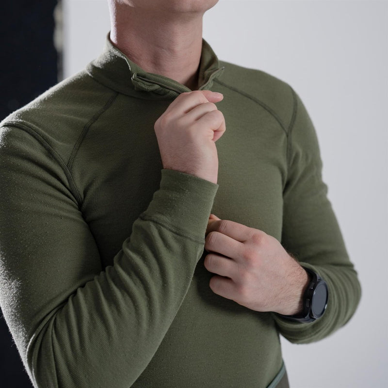 Man wearing olive green Dutch military thermal underwear shirt with high neck and long sleeves, adjusting zipper