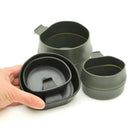 Hand holding genuine Wildo collapsible foldable camping cup showing folded and expanded forms in dark green color.