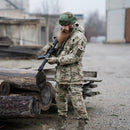 Man wearing Leo Kohler tactical field pants in multicam camouflage holding a rifle outdoors near logs