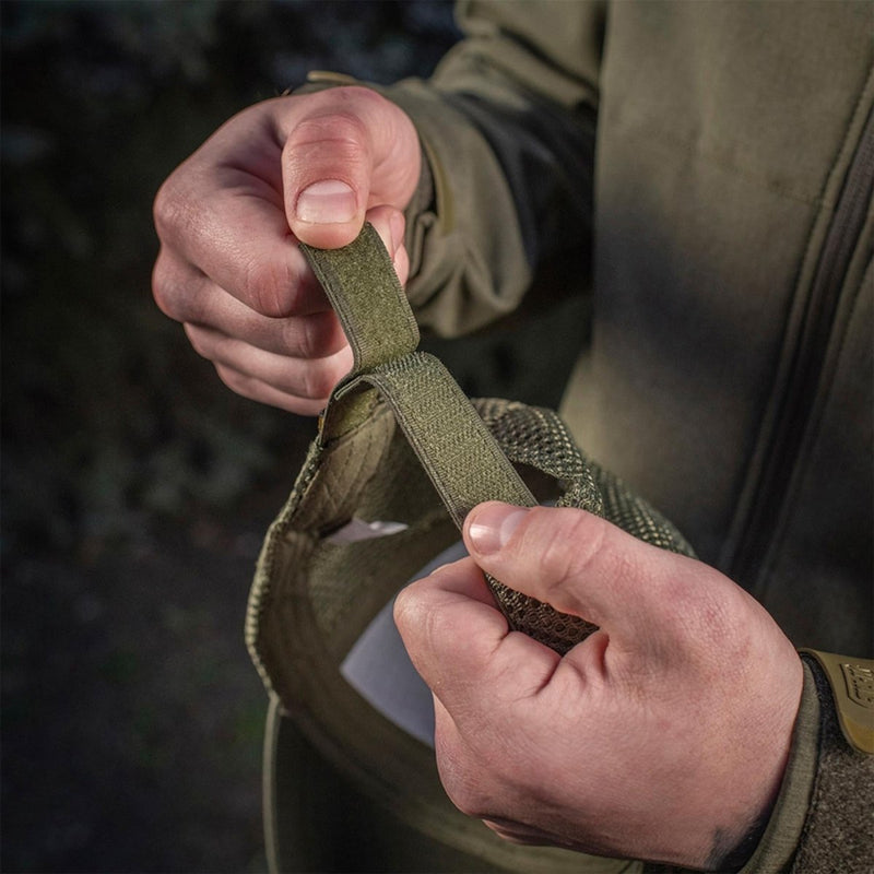Hands adjusting the olive green M-TAC tactical baseball cap's durable hook and loop strap for a custom fit outdoors.