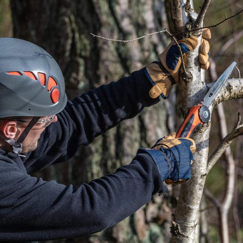 Man wearing safety helmet and gloves using Nordic Pocket Saw to cut a tree branch outdoors