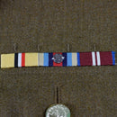 Close-up of British military uniform medal ribbons on a khaki fabric background with a metal button below.
