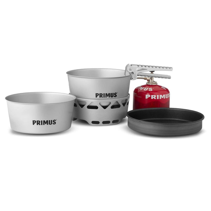 Zestaw kuchenki Primus Essential z garnkiem o pojemności 2,3 l, patelnią i czerwonym kanistrem na paliwo, przeznaczony do uprawiania turystyki pieszej i gotowania na świeżym powietrzu na kempingu