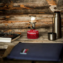 Primus Micron gas lamp lantern with adjustable brightness on red fuel canister next to thermos and books on wooden table